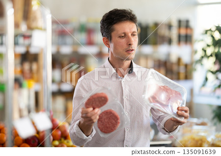 Man in light shirt choose and buy raw cooled beef entrecote and hamburger cutlet in store 135091639