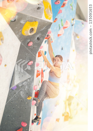 Woman in sportswear practicing rock climbing on climbing wall 135091653
