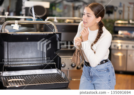 In store, girl inspects mobile grill, buys barbecue device In store, girl inspects mobile grill, buys barbecue device 135091694