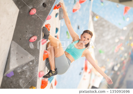 Middle-aged woman climbing on artificial rock wall in rock-climbing gym Middle-aged woman climbing on artificial rock wall in rock-climbing gym 135091696