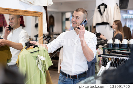 While shopping, man chooses gift, examines womans blouse and talks on phone While shopping, man chooses gift, examines womans blouse and talks on phone 135091700