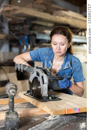 Adult woman saws oak plank in workshop 135091717