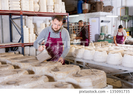 Ceramicist pouring liquid clay into slipcasting molds in pottery workshop Ceramicist pouring liquid clay into slipcasting molds in pottery workshop 135091735