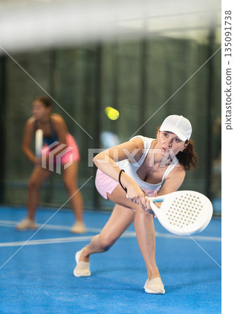 Woman with racket training on outdoor court playing padel game and hitting ball Woman with racket training on outdoor court playing padel game and hitting ball 135091738