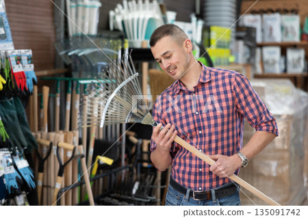 Male gardener choosing rake in hardware store Male gardener choosing rake in hardware store 135091742