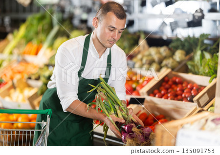 Male seller displaying bunches of purple onions at farmers market 135091753