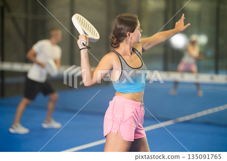 Young woman and man playing tennis against woman 135091765