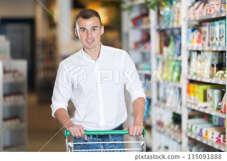 Male shopper with trolley in trading floor browses eco product in bio shop search perfect goods Male shopper with trolley in trading floor browses eco product in bio shop search perfect goods 135091888