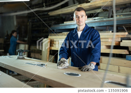 Male sawmill worker cleaning up excess resin or glue on wooden board Male sawmill worker cleaning up excess resin or glue on wooden board 135091906