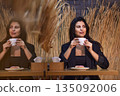 Coffee lover, Wheat theme, Woman indoors. Enjoying cup of coffee, woman sees her reflection in mirror at cafe featuring rustic wheat decor, creating cozy atmosphere. 135092006