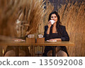 coffee cup, autumn atmosphere, wheat motif. In cozy cafe adorned with wheat decor and warm lighting, woman relaxes with cup coffee, capturing essence autumn. 135092008