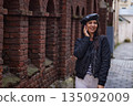 Female portrait, rainy street, smiling woman. Walking near brick wall on rainy day, fashionable woman in black jacket and white pants smiles casually. 135092009