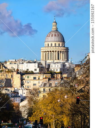Pantheon monument stands in Paris, France. City skyline features the historic dome rising above residential buildings and zinc roofs under a blue sky Pantheon monument stands in Paris, France. City skyline features the historic dome rising above residential buildings and zinc roofs under a blue sky 135092167