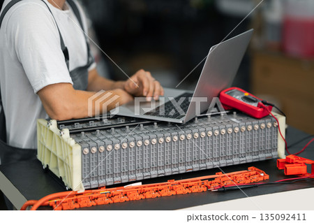 Serviceman repairs electric battery pack of hybrid car using laptop Serviceman repairs electric battery pack of hybrid car using laptop 135092411