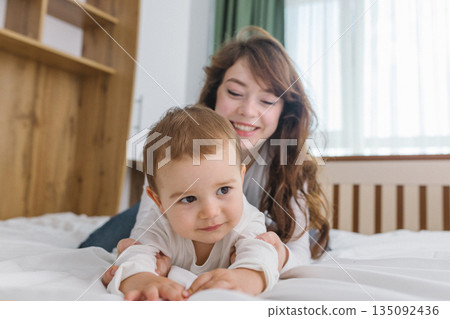 Young mother playing with her baby at home, enjoying a warm and cozy family moment full of tenderness, comfort, natural light, and playful parent-child connection. 135092436