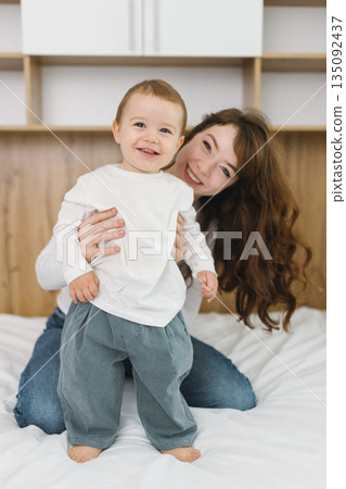 Young mother playing with her baby at home, enjoying a warm and cozy family moment full of tenderness, comfort, natural light, and playful parent-child connection. 135092437
