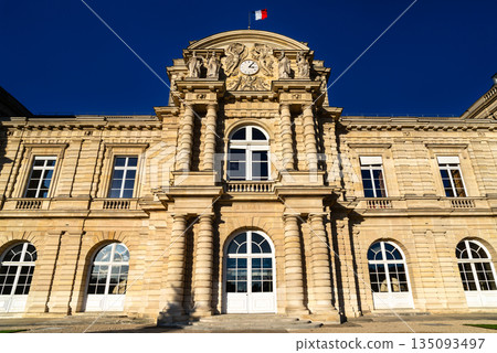 Luxembourg Palace stands in the Jardin du Luxembourg in Paris, France. Historic stone facade of the French Senate building features columns and a clock under a blue sky 135093497