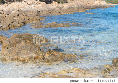 Rocky Mediterranean shoreline with clear blue water and natural stone textures. Sunny summer day, calm sea and untouched coastal landscape. Ideal for travel, nature and vacation concepts., La 135094141