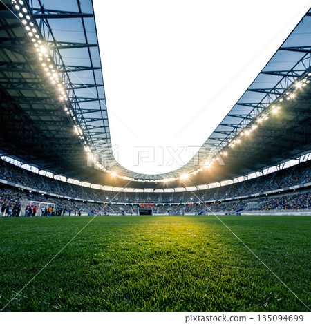 Wide-angle view of a soccer stadium filled with fans during an evening match with bright lights shining above the field 135094699