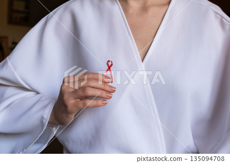 A doctor holds a red ribbon in their hand, symbolizing awareness for World Cancer Day on February 4th. The doctor wears a white coat and shows commitment to cancer awareness. A doctor holds a red ribbon in their hand, symbolizing awareness for World Cancer Day on February 4th. The doctor wears a white coat and shows commitment to cancer awareness. 135094708