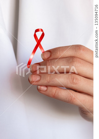 A doctor holds a red ribbon in their hand, symbolizing awareness for World Cancer Day on February 4th. The doctor wears a white coat and shows commitment to cancer awareness. A doctor holds a red ribbon in their hand, symbolizing awareness for World Cancer Day on February 4th. The doctor wears a white coat and shows commitment to cancer awareness. 135094716