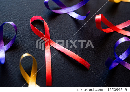 Red ribbon on a black background symbolizes World Cancer Day on February 4th. Additional ribbons in various colors are also present, representing different cancers. Red ribbon on a black background symbolizes World Cancer Day on February 4th. Additional ribbons in various colors are also present, representing different cancers. 135094849