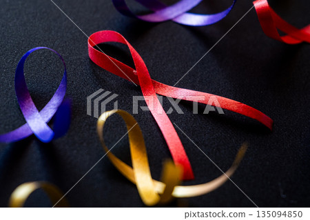 Red ribbon on a black background symbolizes World Cancer Day on February 4th. Additional ribbons in various colors are also present, representing different cancers. Red ribbon on a black background symbolizes World Cancer Day on February 4th. Additional ribbons in various colors are also present, representing different cancers. 135094850