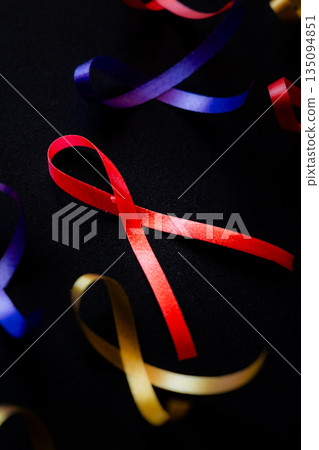 Red ribbon on a black background symbolizes World Cancer Day on February 4th. Additional ribbons in various colors are also present, representing different cancers. 135094851