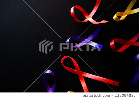 Red ribbon on a black background symbolizes World Cancer Day on February 4th. Additional ribbons in various colors are also present, representing different cancers. Red ribbon on a black background symbolizes World Cancer Day on February 4th. Additional ribbons in various colors are also present, representing different cancers. 135094853
