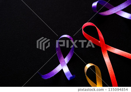 Red ribbon on a black background symbolizes World Cancer Day on February 4th. Additional ribbons in various colors are also present, representing different cancers. Red ribbon on a black background symbolizes World Cancer Day on February 4th. Additional ribbons in various colors are also present, representing different cancers. 135094854