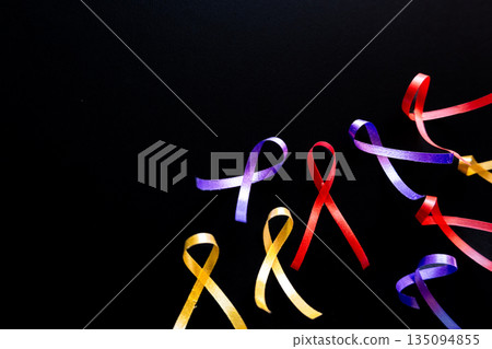 Red ribbon on a black background symbolizes World Cancer Day on February 4th. Additional ribbons in various colors are also present, representing different cancers. 135094855