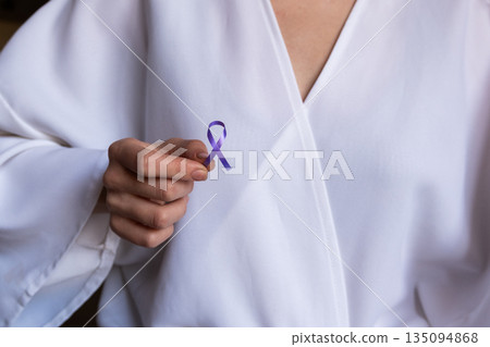 A doctor holds a purple ribbon symbolizing cancer awareness. The doctor is wearing a white coat, emphasizing the medical context of World Cancer Day on February 4th. 135094868