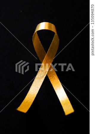 Gold ribbon on a black background symbolizing International Childhood Cancer Day on February 15th. The ribbon is elegantly shaped and prominently displayed. Gold ribbon on a black background symbolizing International Childhood Cancer Day on February 15th. The ribbon is elegantly shaped and prominently displayed. 135094870
