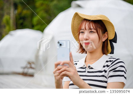 一名女子在圓頂帳篷內以智慧型手機拍照（照片由沖繩海濱度假村雅提供） 135095074