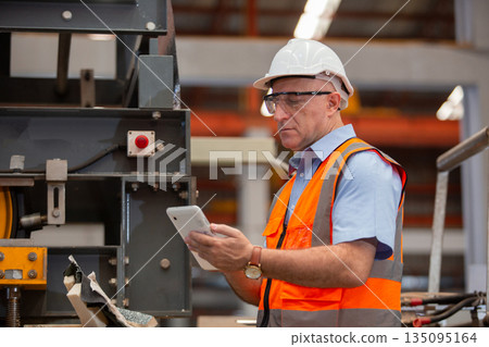 Experienced factory engineer in safety vest and helmet using tablet to inspect industrial equipment at production plant. Concept of digital technology in modern manufacturing operations. Experienced factory engineer in safety vest and helmet using tablet to inspect industrial equipment at production plant. Concept of digital technology in modern manufacturing operations. 135095164