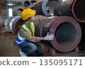 Female industrial worker wearing uniform safety helmet and reflective vest inspects metal coil in factory warehouse, highlighting quality control, Check product quality manufacturing operations. 135095171