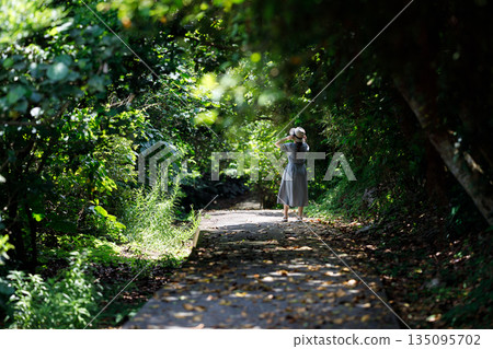A woman walking along a forest path surrounded by greenery 135095702