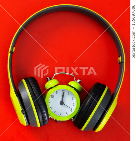 Headphones surrounding green alarm clock on red background Headphones surrounding green alarm clock on red background 135097606