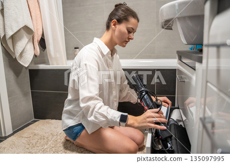 A woman prepares a hair dryer while sitting on the bathroom floor at home. Real life interior scene showing personal care routine, household organization and everyday domestic life A woman prepares a hair dryer while sitting on the bathroom floor at home. Real life interior scene showing personal care routine, household organization and everyday domestic life 135097995