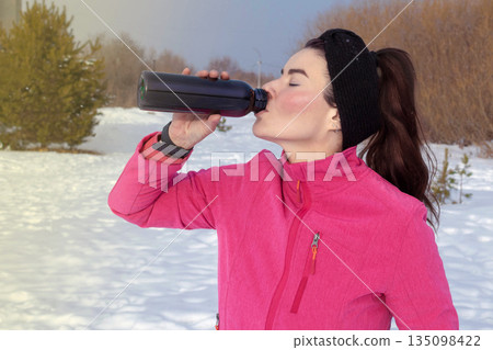 Caucasian woman goes in for outdoor sports in winter. Woman drinks clean water from bottle. Portrait close up 135098422