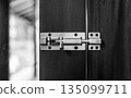 A close-up shot of a silver metal sliding barrel bolt lock installed on a dark wooden door, showing the security hardware in a locked position 135099711