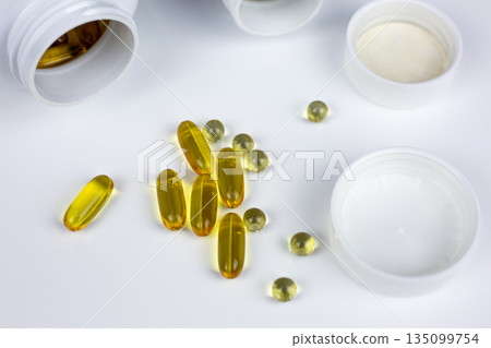 Omega-3 fatty acid dietary supplement capsules, along with vitamin D3 and K2, are scattered on white table near jars. Valuable marine fish oil in softgel capsules to increase Omega-3 level in body Omega-3 fatty acid dietary supplement capsules, along with vitamin D3 and K2, are scattered on white table near jars. Valuable marine fish oil in softgel capsules to increase Omega-3 level in body 135099754