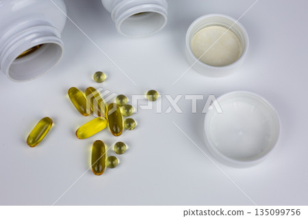 Yellow capsules with Omega 3 and D3 vitamins. Set of dietary supplements on white background. Scattered tablets. Concept of taking vitamins in capsules and tablets 135099756
