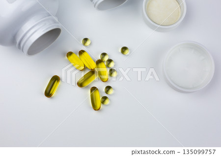 Fish oil capsules. Dietary supplements are scattered across white table, isolated. Set of vitamins for dietary supplements. White table with vitamin capsules and jars 135099757
