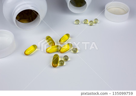 Various types of dietary supplements spill out of jars on white background. Yellow capsules with gelatin membrane for taking vitamins with food. Improving health and wellbeing 135099759