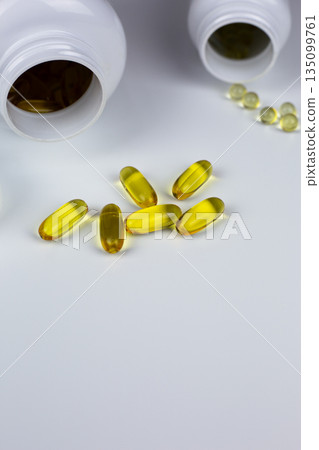 Vertical photo of Omega 3 and vitamin D3 capsules with K2 on white background near jars. Dietary supplements for improving wellbeing. Capsules with set of vitamins for improving health Vertical photo of Omega 3 and vitamin D3 capsules with K2 on white background near jars. Dietary supplements for improving wellbeing. Capsules with set of vitamins for improving health 135099761