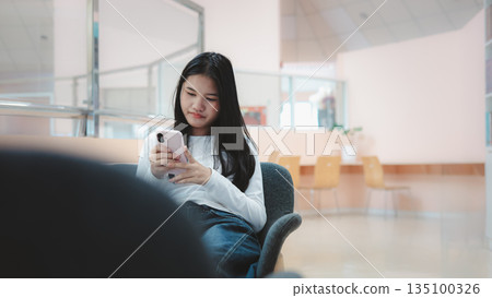 Asian woman using smartphone in modern coworking space or office lounge Asian woman using smartphone in modern coworking space or office lounge 135100326