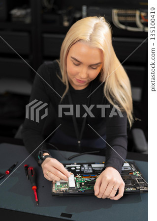 Woman IT technician works on laptop hardware during repair and upgrade in a workshop Woman IT technician works on laptop hardware during repair and upgrade in a workshop 135100419