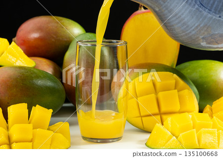 Freshly squeezed mango juice pouring from a jug into a glass. 135100668