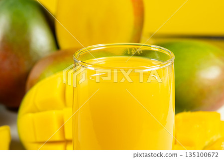 Glass of fresh mango juice surrounded by whole and sliced fruits. 135100672